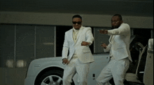 two men in white suits standing next to a white car