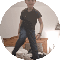 a boy in a black shirt and blue jeans jumps on a bed