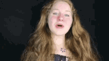 a woman with long red hair and a purple necklace is crying .