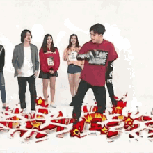 a group of people are standing around a man in a red shirt who is standing in front of a pile of balloons .