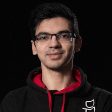 a man wearing glasses and a black hoodie is standing in front of a black background .
