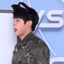a young man wearing a cat ear headband stands in front of a sign that says ' s '