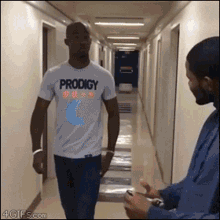 a man wearing a white prodigy shirt walking down a hallway