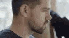 a man with a beard is sitting in front of a window looking out .
