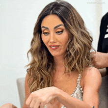 a woman with long wavy hair is sitting in front of a white wall with a caption that says colucciyrange