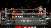 two wrestlers are standing in a wrestling ring with a referee and a crowd watching .