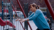 a woman in a blue sweater is playing on a swing set in a park sponsored by state farm
