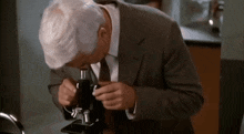 a man in a suit and tie is looking through a microscope in a laboratory .