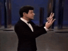 a man in a tuxedo and bow tie is making a peace sign .