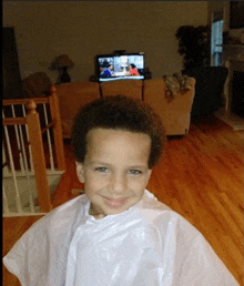 a young boy wearing a white plastic cape is smiling in front of a television