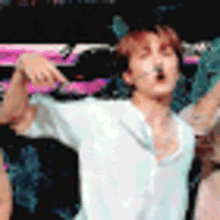 a man in a white shirt is standing on a stage with his arms outstretched and a microphone in his mouth .