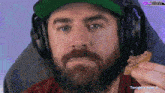 a man with a beard wearing headphones and a hat eating a cookie