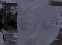 a woman is standing in front of a white house with a ghost hanging from a clothesline