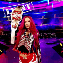 a woman with red hair is standing on a stage holding a wrestling championship belt .