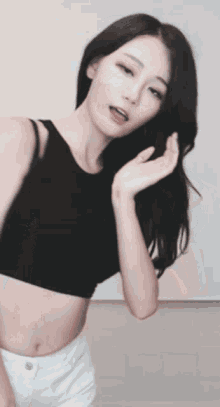 a woman in a black crop top and white shorts is dancing in front of a white wall .