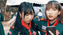 two girl scouts looking at a cell phone with the word fever on the bottom right