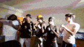 a group of young men are dancing in a room and one of them is wearing a yellow hat