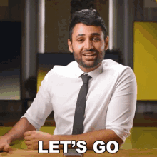 a man in a white shirt and black tie is sitting at a table and says let 's go