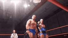 two wrestlers are standing in a wrestling ring with a referee in the background