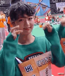 a girl in a green sweater is holding a sign that says ' heyyo ' on it .