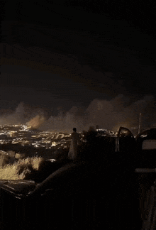 a man stands on a hill looking at a fire in the distance