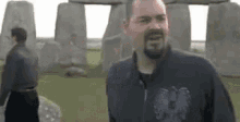 a man with a beard is standing in front of a stone wall and talking to another man .