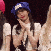 a girl wearing a blue hat and a white shirt is standing next to a girl wearing a pink hat