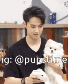 a young man is holding a small white dog in his arms while using his phone ..