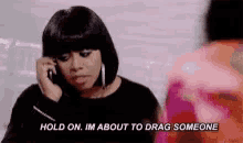a woman is talking on a cell phone and saying `` hold on . im about to drag someone '' .