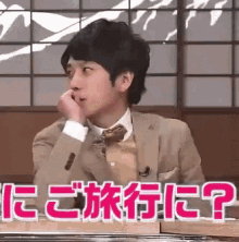 a man in a suit and tie is sitting at a table with his hand to his mouth and the words in a foreign language .