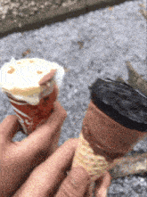 a person is holding a cup of ice cream next to a chocolate cone