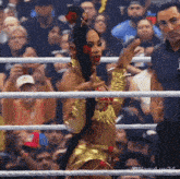 a woman in a gold outfit is standing in a boxing ring with a crowd watching