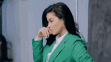 a woman in a green jacket and white shirt is covering her nose with her hand