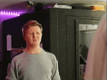 a man in a grey shirt stands in front of a safe with a purple light behind him