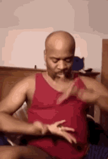 a man in a red tank top is holding a woman 's hand while sitting on a bed .