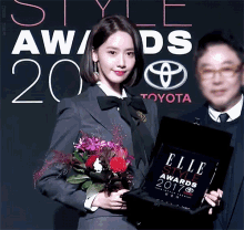 a woman in a suit is holding flowers and a box that says elle style awards
