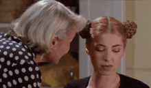 a woman in a polka dot shirt is touching another woman 's head