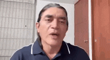 a man with long hair is talking on a video call in a room .