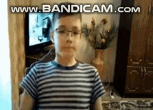 a young boy wearing glasses and a striped shirt is sitting in front of a television in a living room .