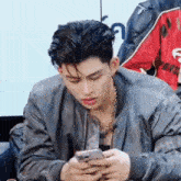 a young man in a jacket is looking at his cell phone .
