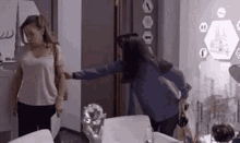 two women are standing next to each other in a living room . one of the women is holding the door open .