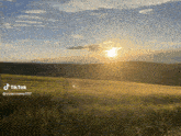 a tiktok video of a field with the sun setting in the background