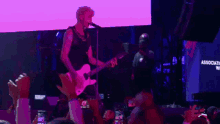 a man is playing a guitar and singing into a microphone while a crowd watches .