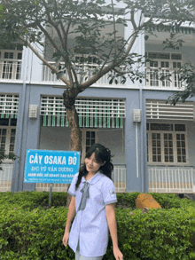 a girl stands in front of a building with a sign that says " cây osaka bo "