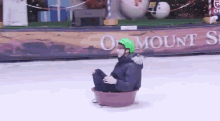 a person wearing a green helmet is riding a sled on a snowy surface .