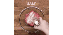a person is pouring salt into a bowl of meat on a wooden table .