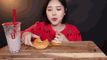 a woman in a red shirt is eating a donut next to a cup of milk