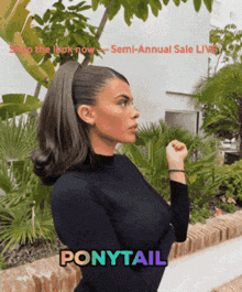 a woman wearing a ponytail is standing in front of a garden