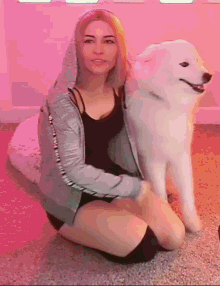a woman is kneeling down next to a white dog with a pink background