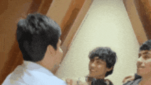 a group of young men are standing in front of a mirror talking to each other